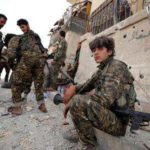 A fighter from Syrian Democratic Forces sits on a curb as he holds his weapon in Raqqa